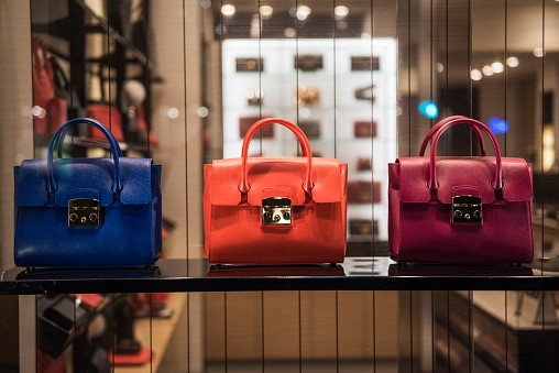 A blue, orange and pink purse in a retail window display on a shelf.
