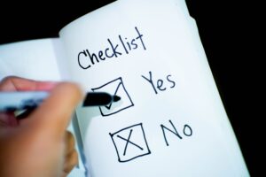 Hand writing a checklist in a notepad with a "yes" box with a check and a "no" box with an "x."
