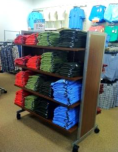 Clothing shelves in a retail store holding red, green, black and blue t-shirts.