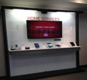 Floating shelf display with technology items below a flat screen tv with a red screen and "HOME SERVICES" sign.