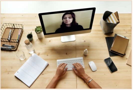 Hands typing on a computer at a desk surrounded by desk items while video conferencing.