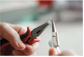 Two hands building a jewelry piece with pliers.