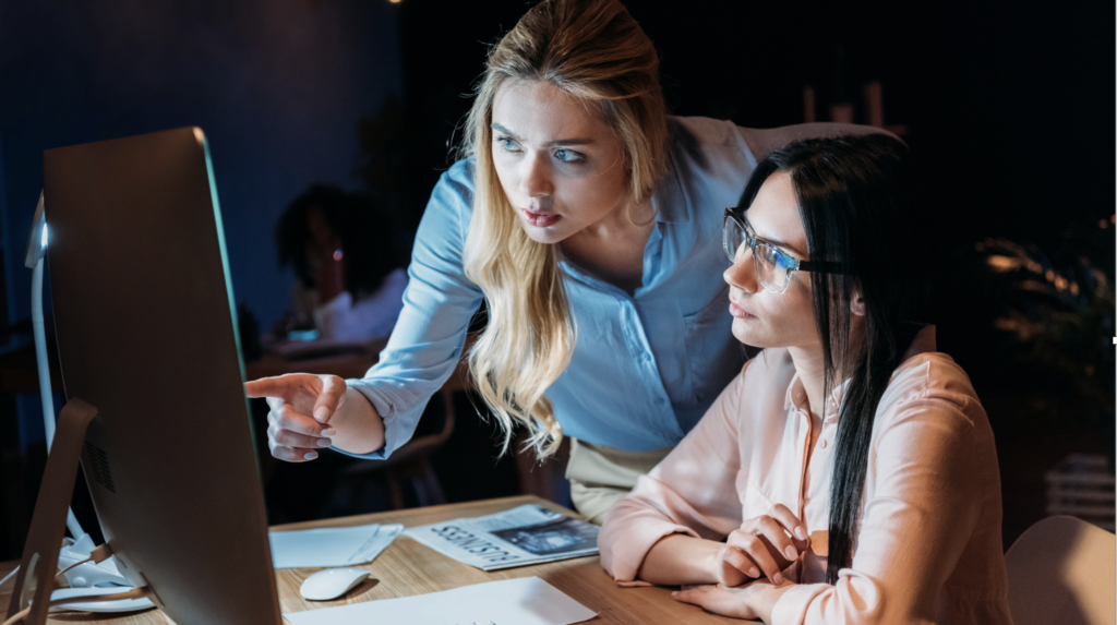 Women looking at something on a bright desktop computer screen.