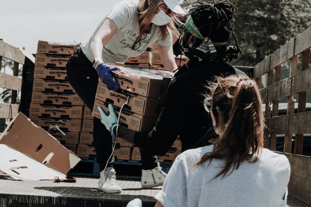 Woman in a mask handing boxes of fruit down from a truck.