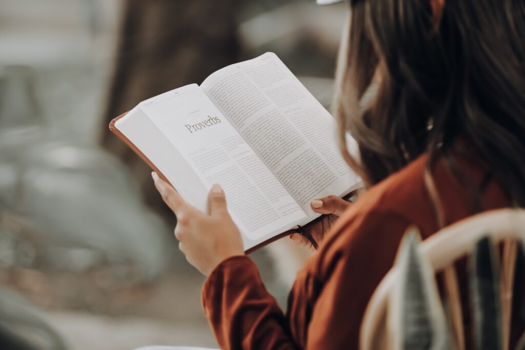 Woman sitting in a chair, reading a Bible from behind