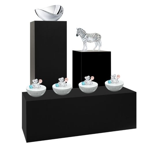 Black pedestals in multiple sizes and shapes showcasing glass animals and a glass bowl.