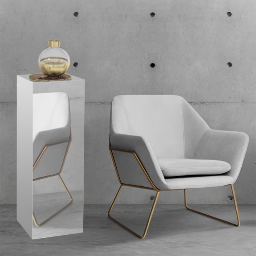 Seating area with mirrored display pedestal with a vase on top, next to a gray and gold modern chair.