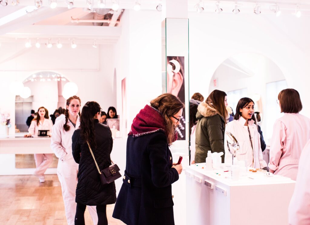 People shopping a well lighted pink beauty counter