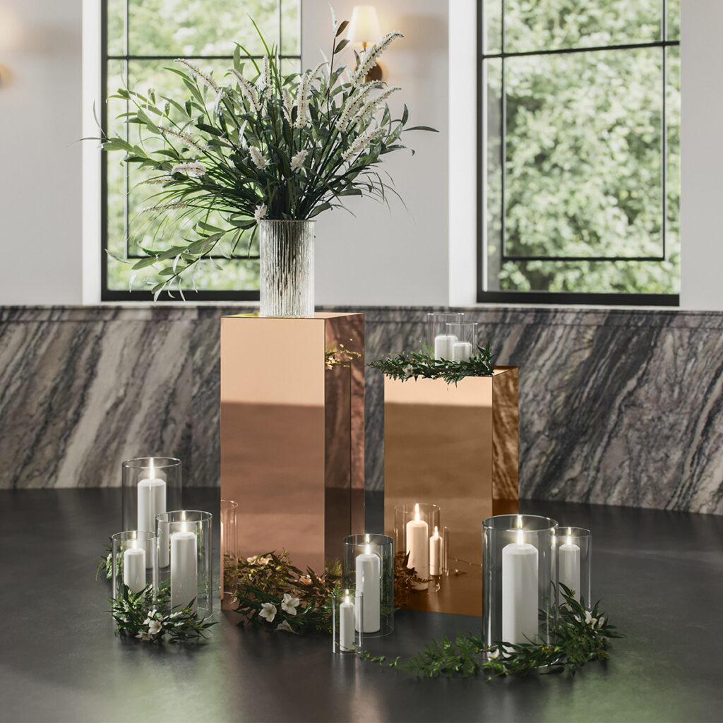 Mirrored Pedestals with greenery and candles surrounding it.