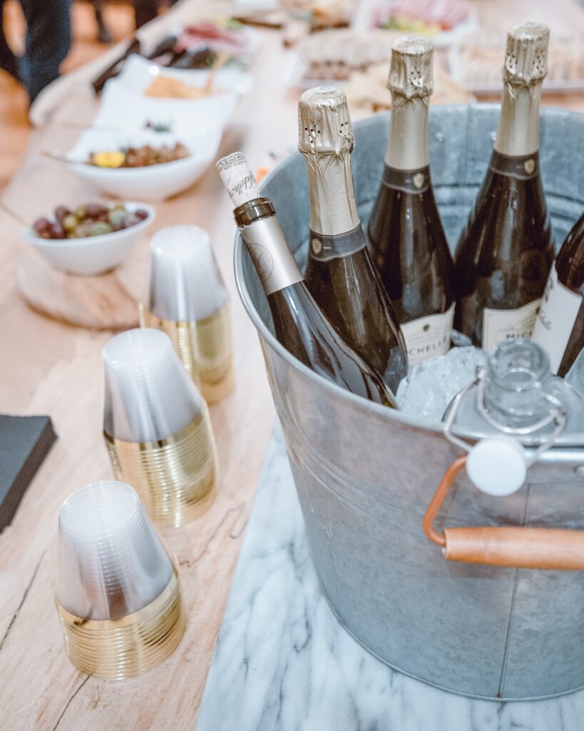 Drink and food table at a party with a bucket of wine.